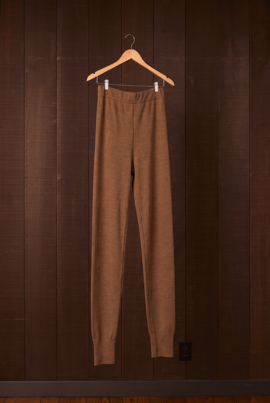 Tall women's walnut brown merino wool leggings on a hanger against a dark wooden wall
