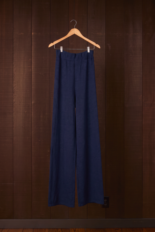 Tall women's indigo merino wool wide-leg pants on a hanger against a dark wooden wall