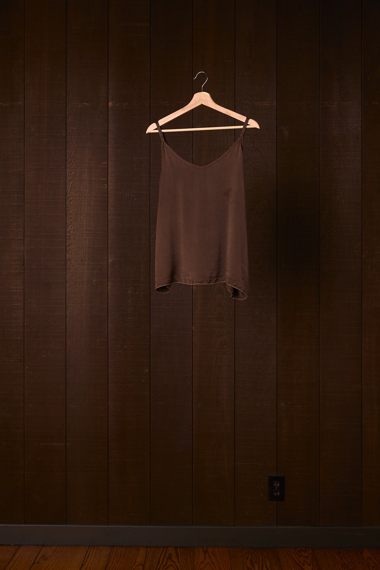 Brown silk tank top on a hanger against a dark wooden wall.