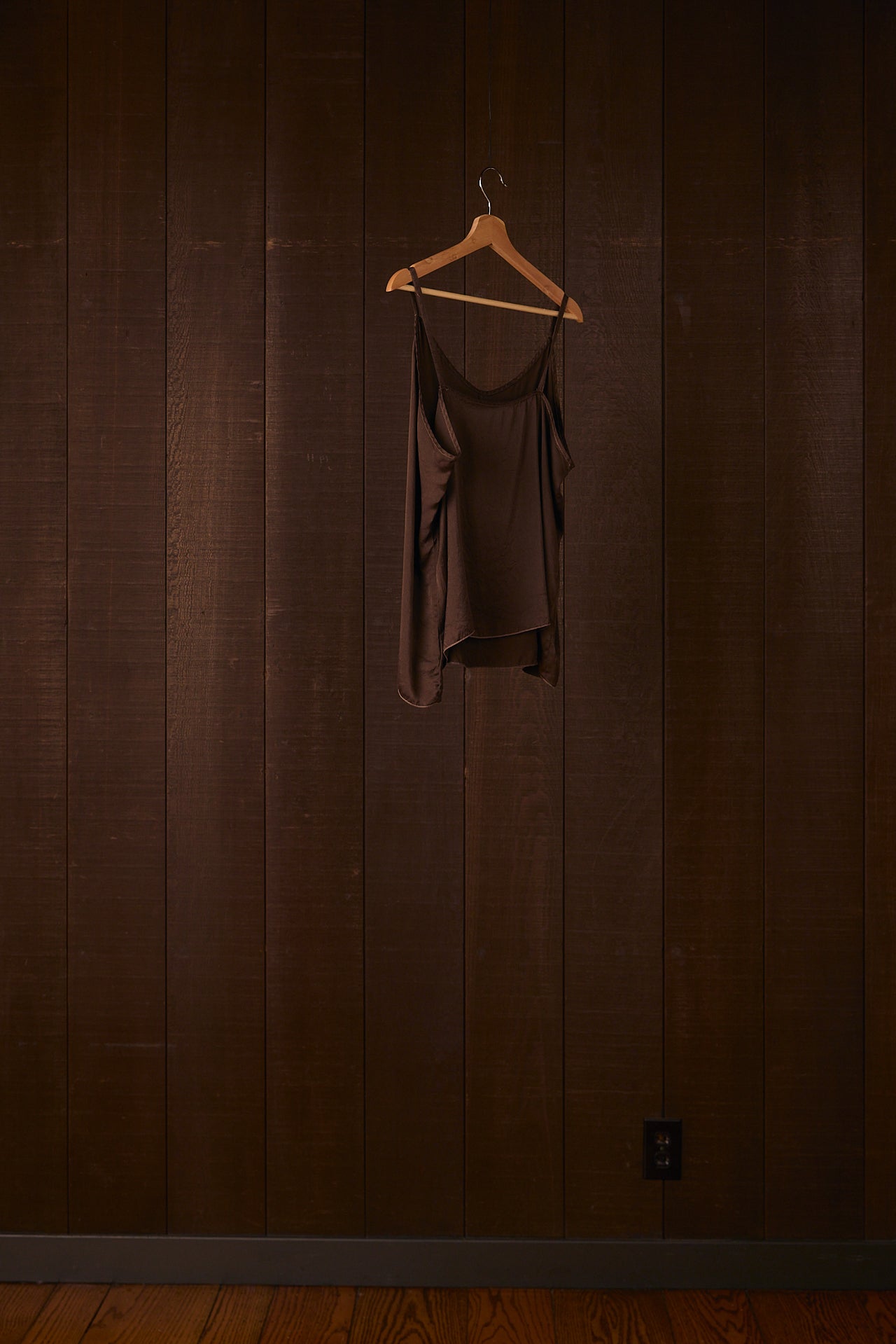 Plant dyed silk camisole hanging on a wooden hanger against a dark brown wall.