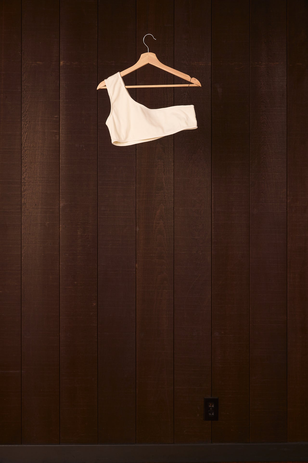 White bra on a wooden hanger against a dark wooden wall.
