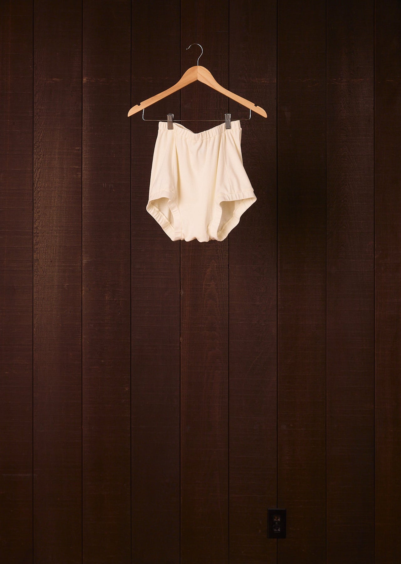 White baby romper on a wooden hanger against a dark wooden wall.