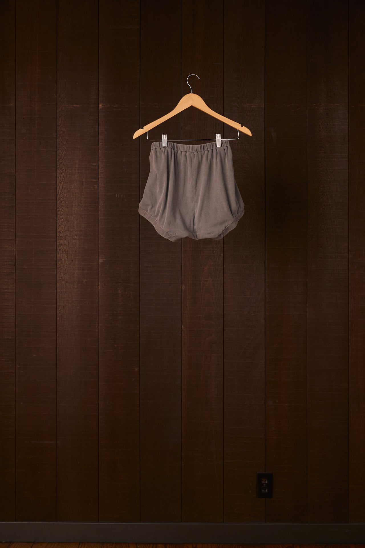Gray shorts on a wooden hanger against a dark wooden wall.