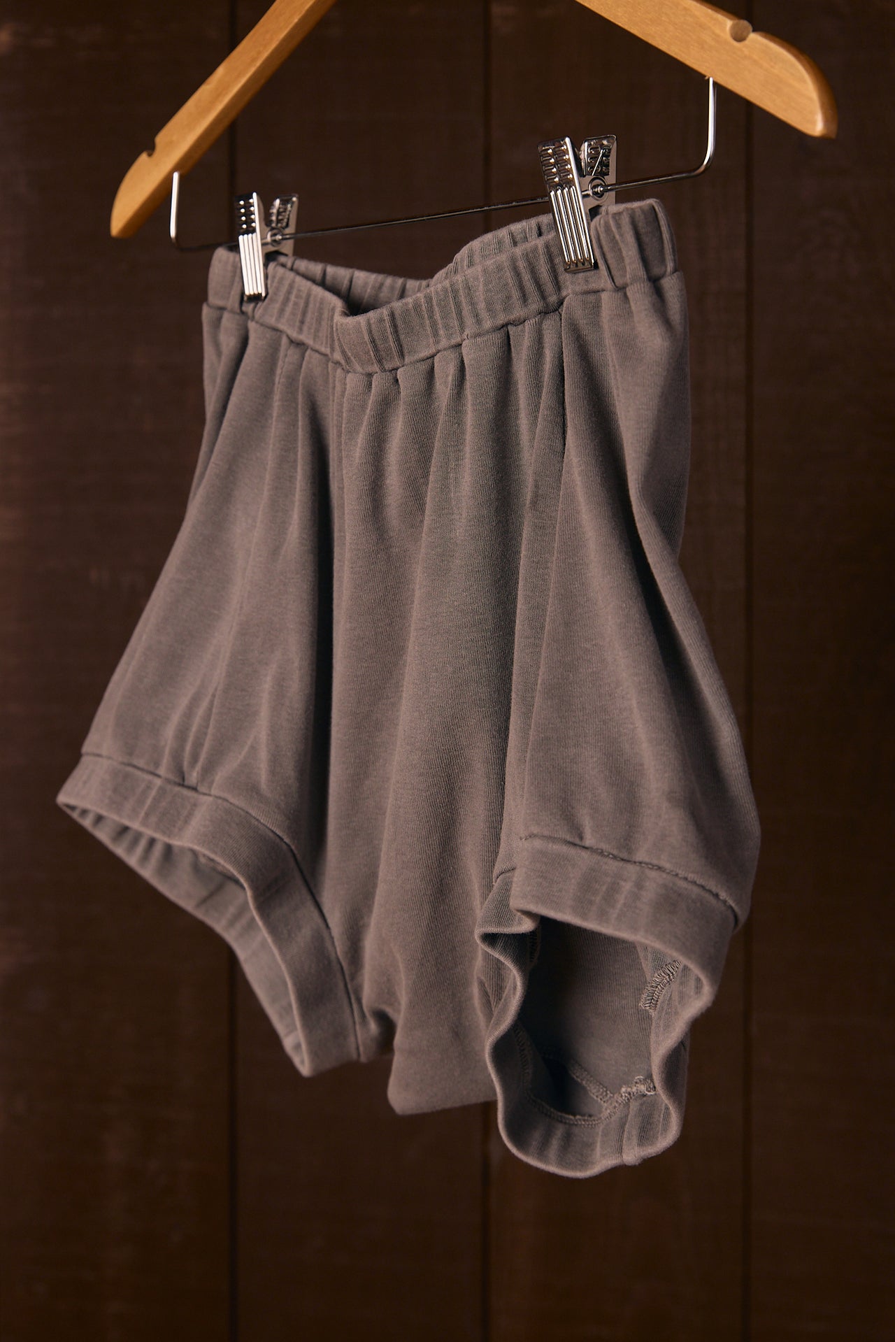 Tall women's gray shorts hanging on a wooden hanger against a dark background