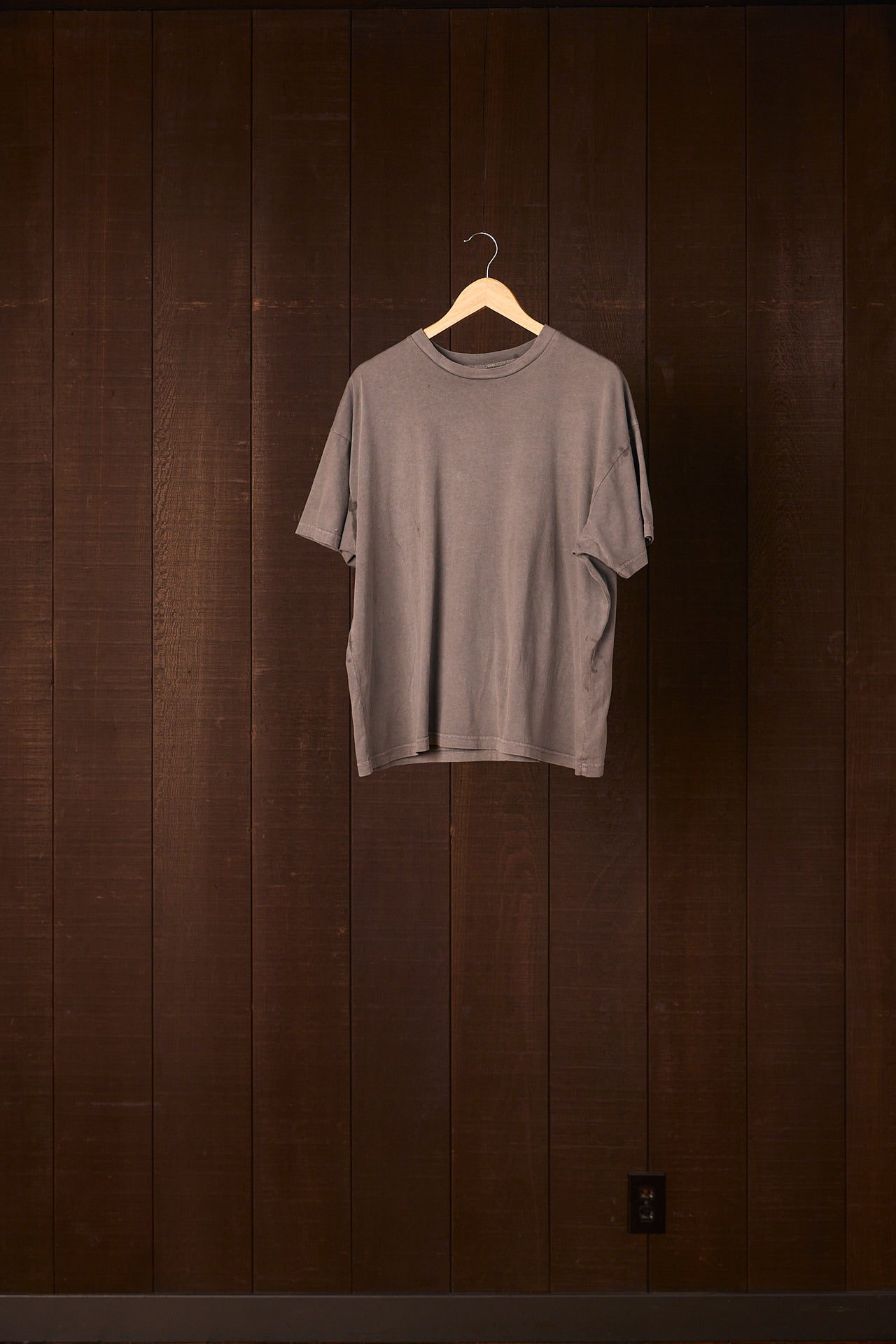 OurCarbon dyed gray t-shirt on a hanger against a dark wooden wall