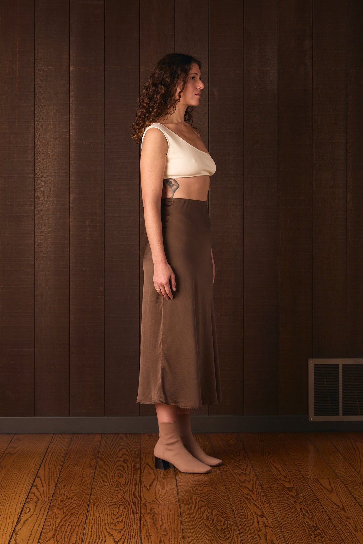 Una Bra worn, standing against a brown wall (shown undyed for fit)