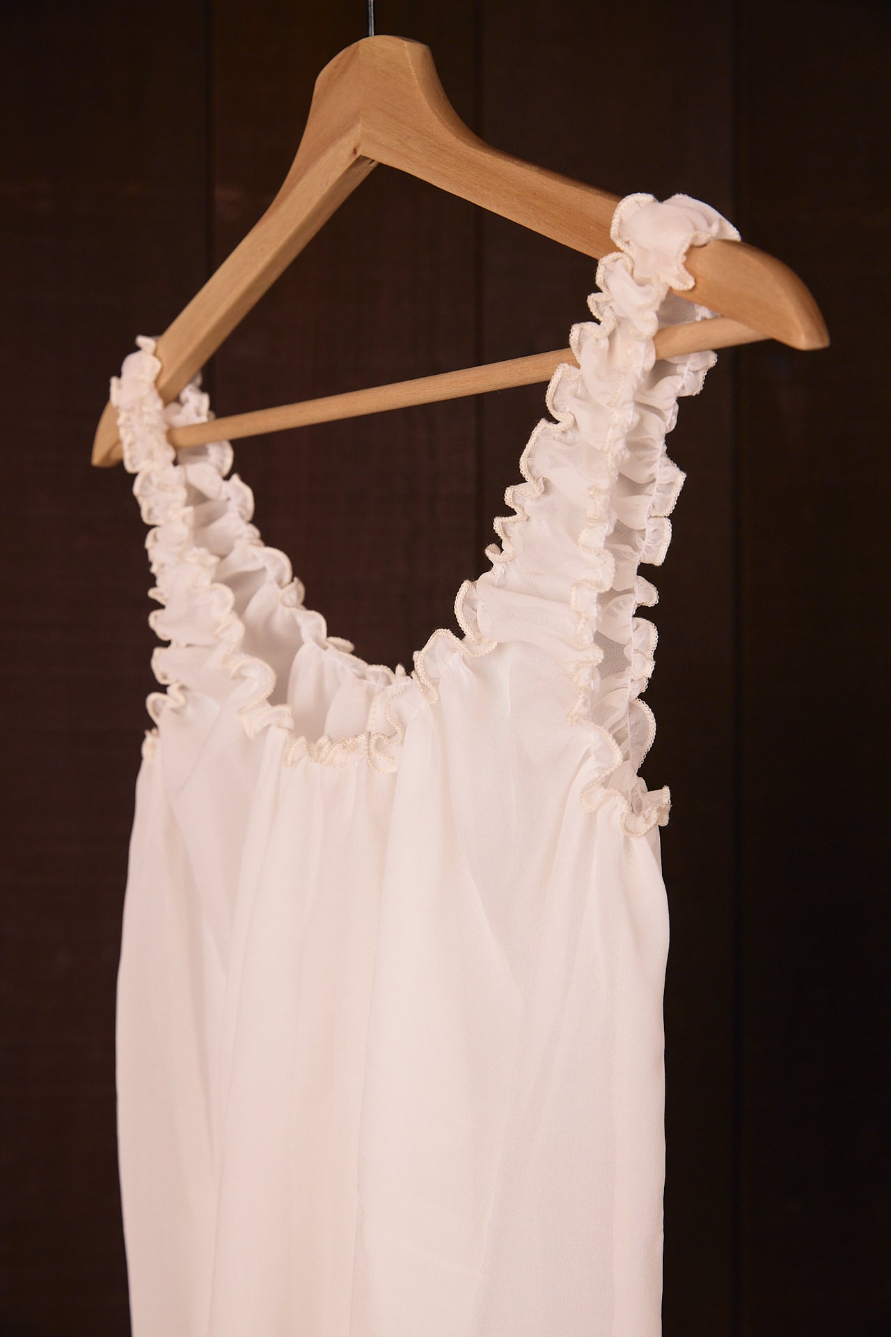 Silk sleeveless top on a wooden hanger against a dark background