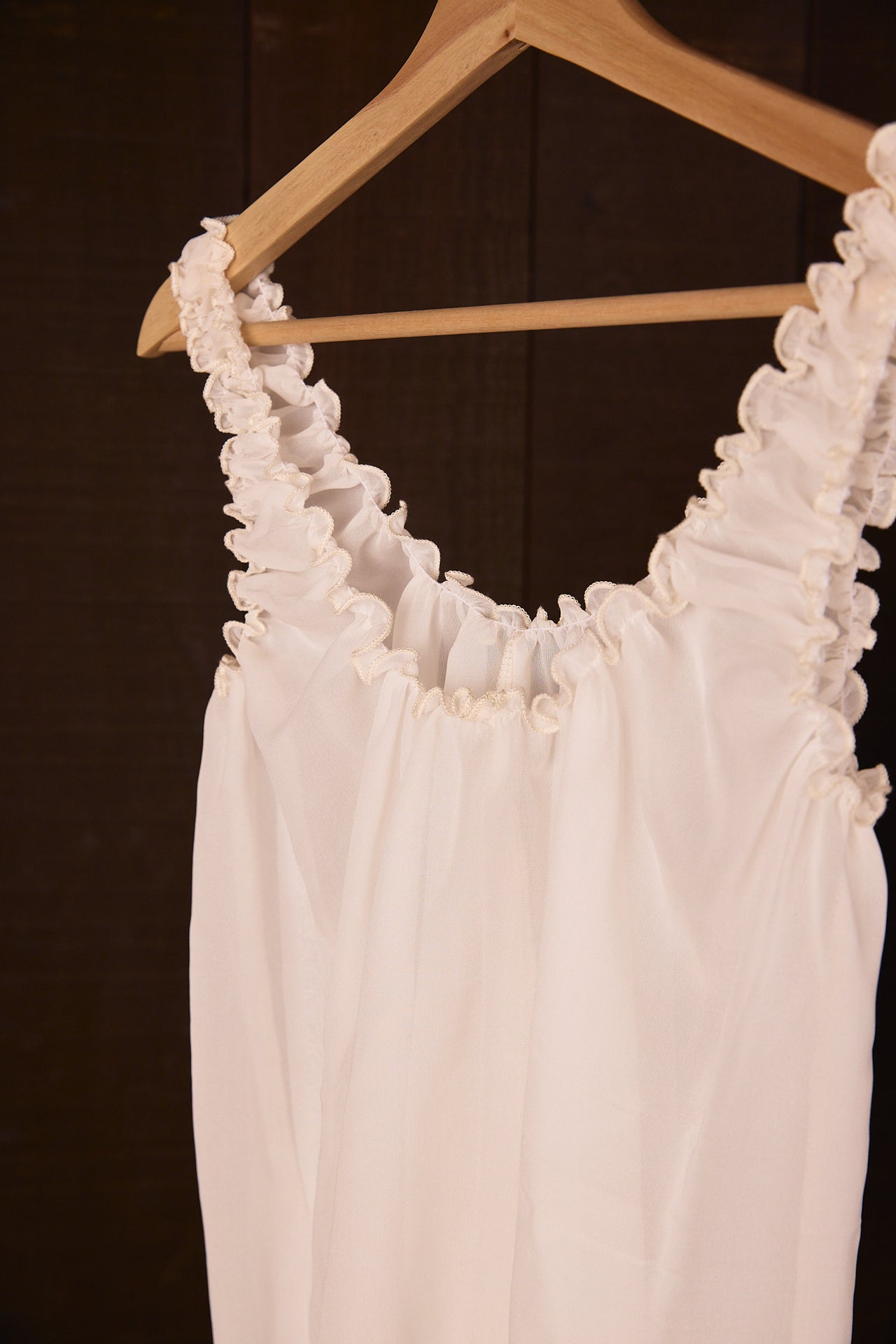 Silk chiffon tank top on a wooden hanger against a dark background