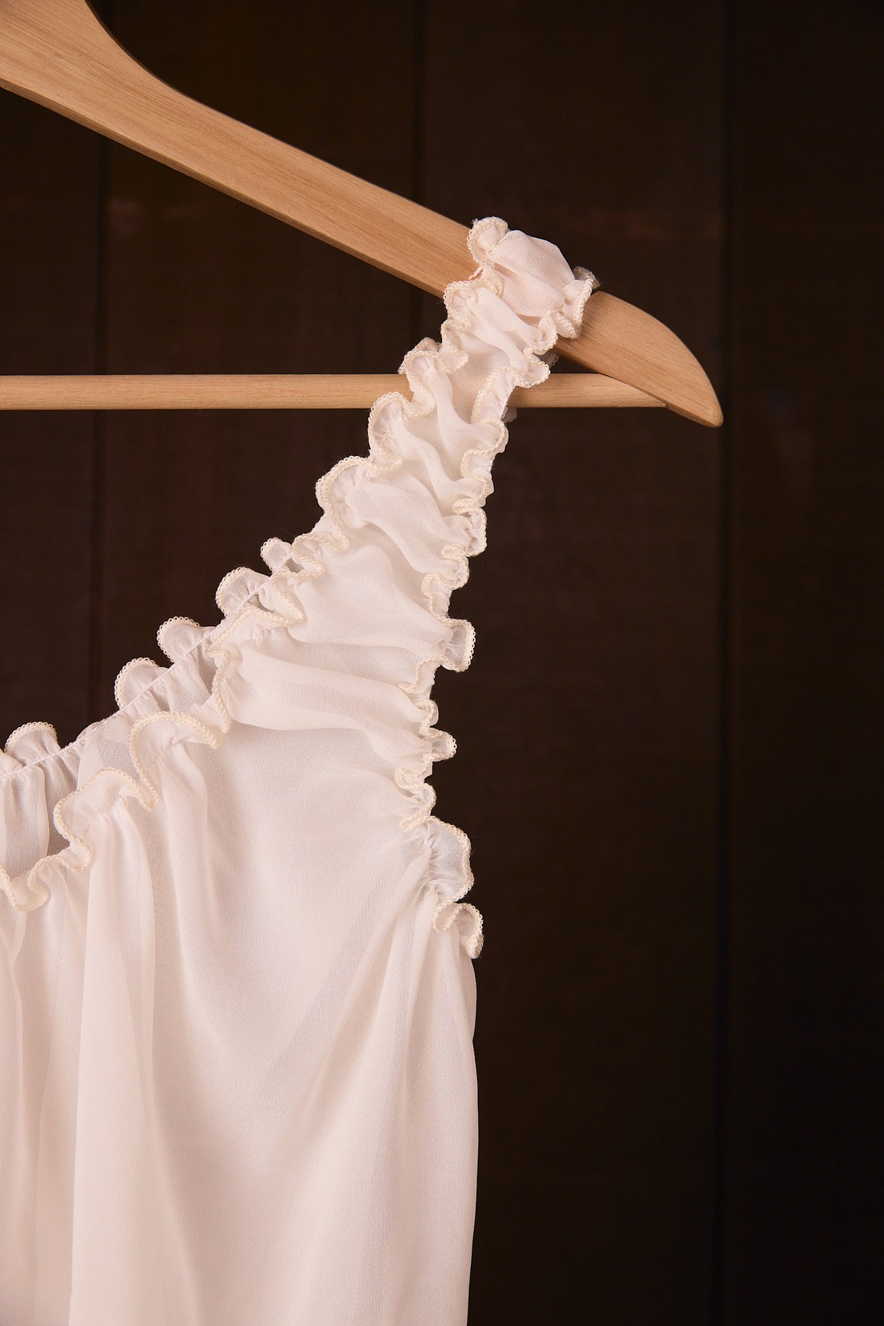 Silk chiffon top on a wooden hanger against a dark background