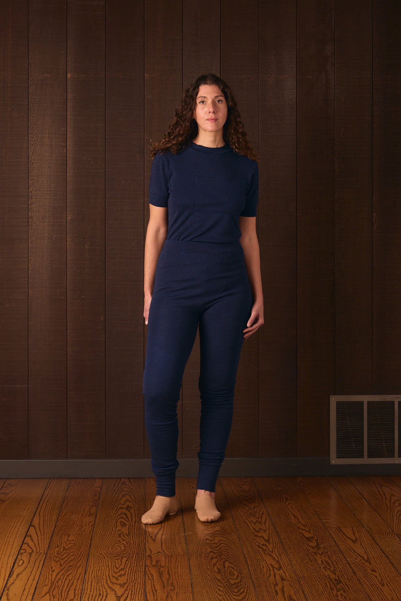 Herderin model wearing an indigo blue outfit standing against a brown wall.