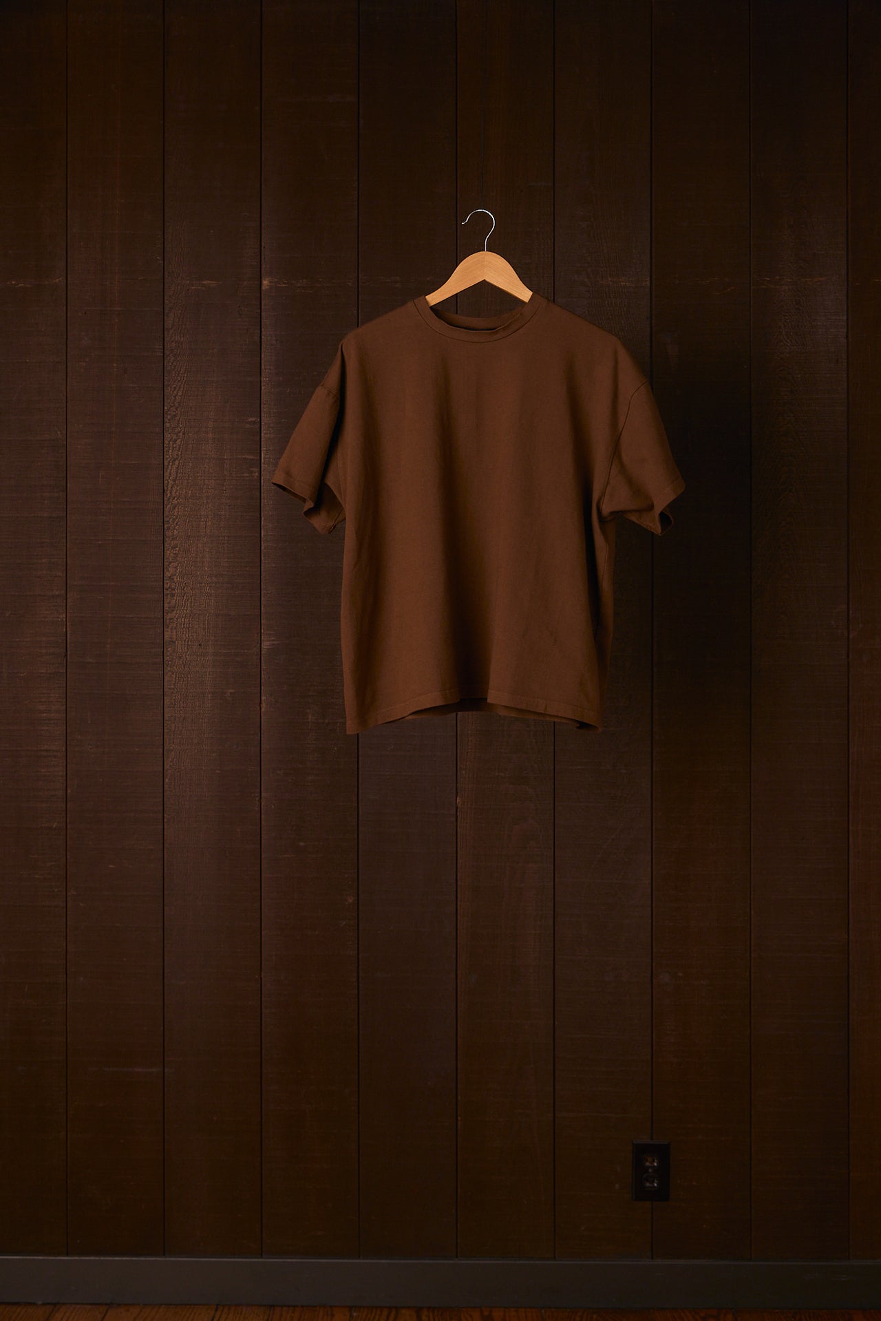 Brown t-shirt on a hanger against a wooden wall.