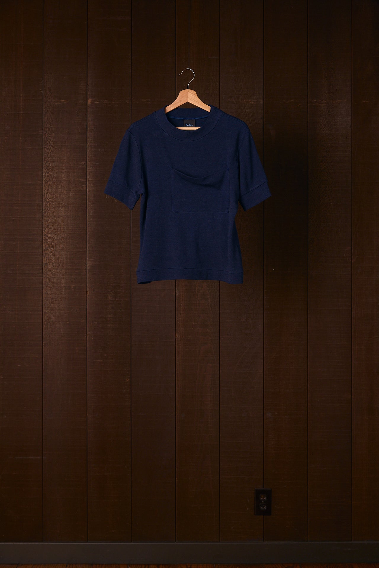 Navy blue merino wool top on a hanger against a wooden wall.