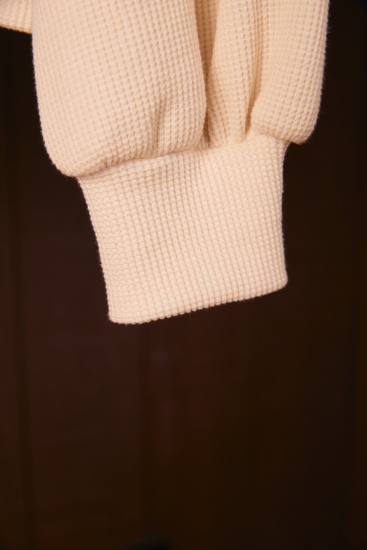 Close-up of a beige waffleknit sweater cuff on a dark background