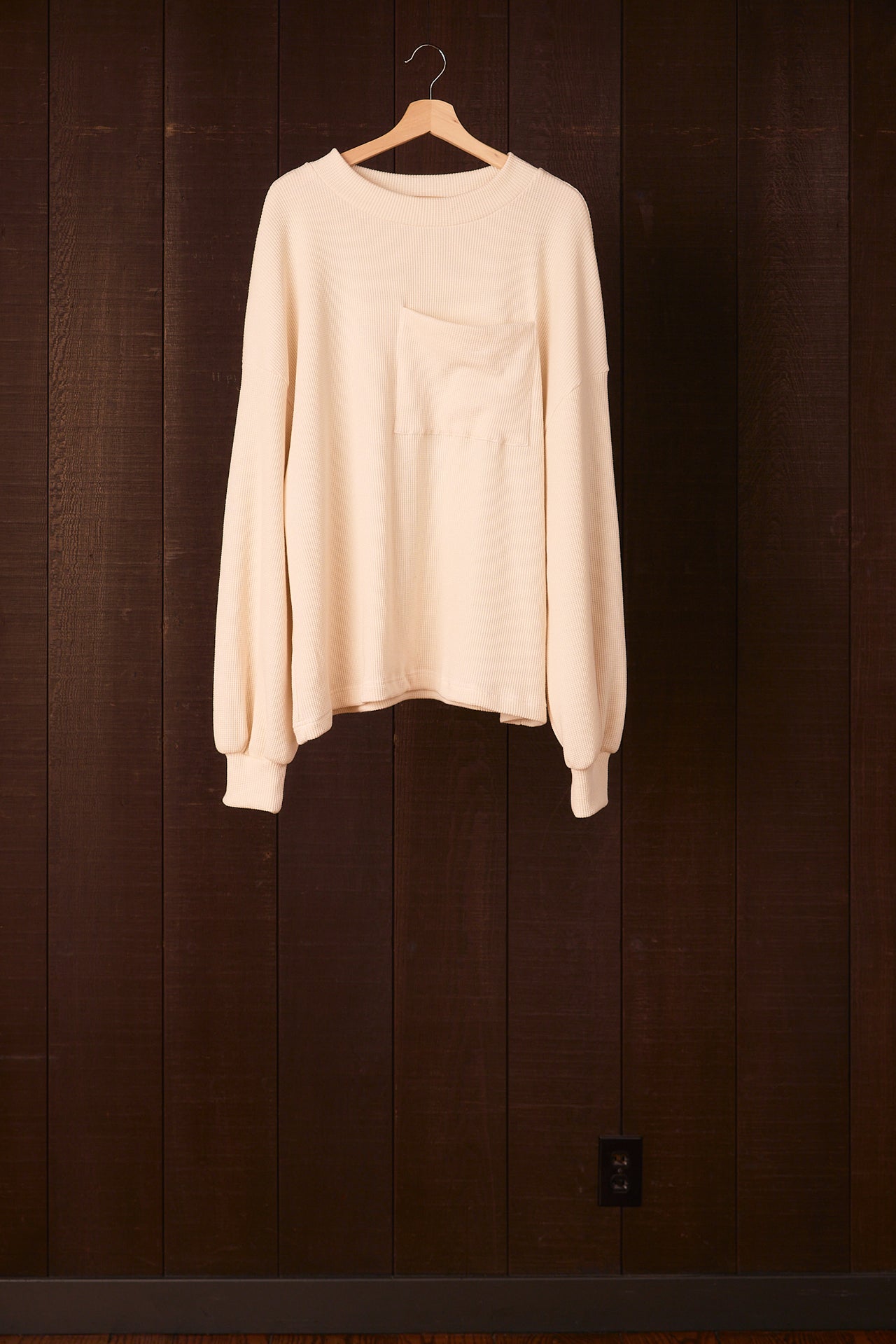 Tall women's sweater hanging on a wooden hanger against a dark wooden panel background