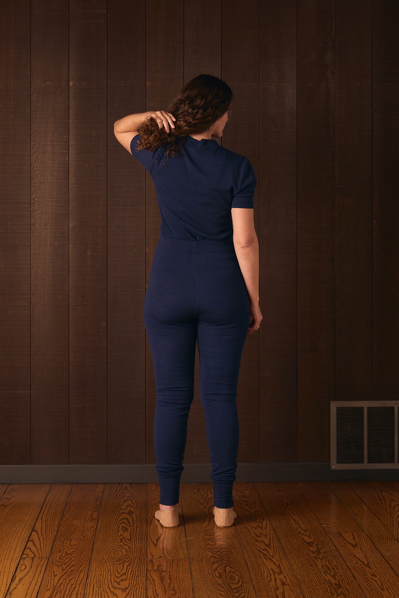 Person wearing a blue outfit standing against a brown wall.