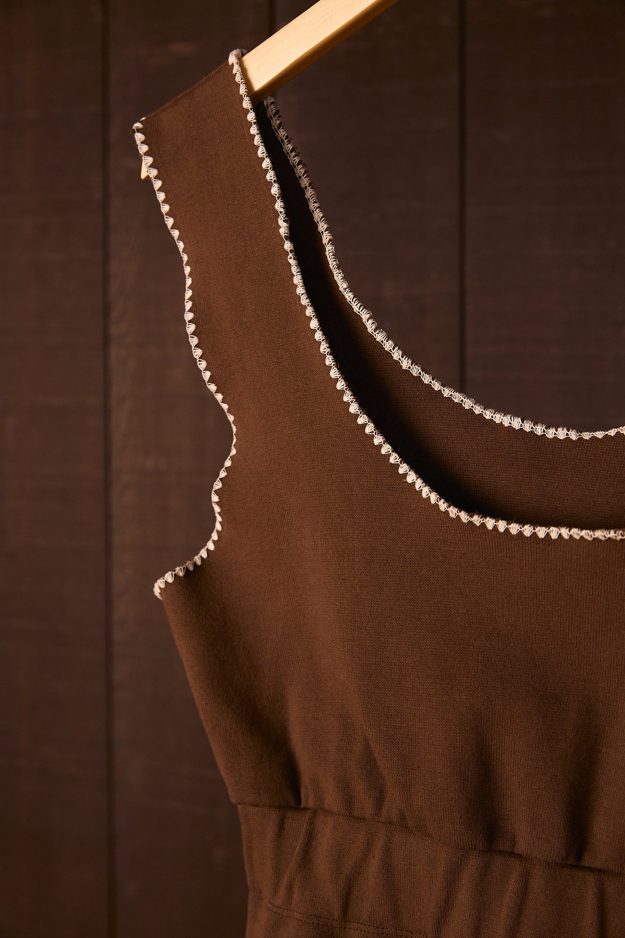 Brown crop top with shell stitch on a wooden hanger against a brown background