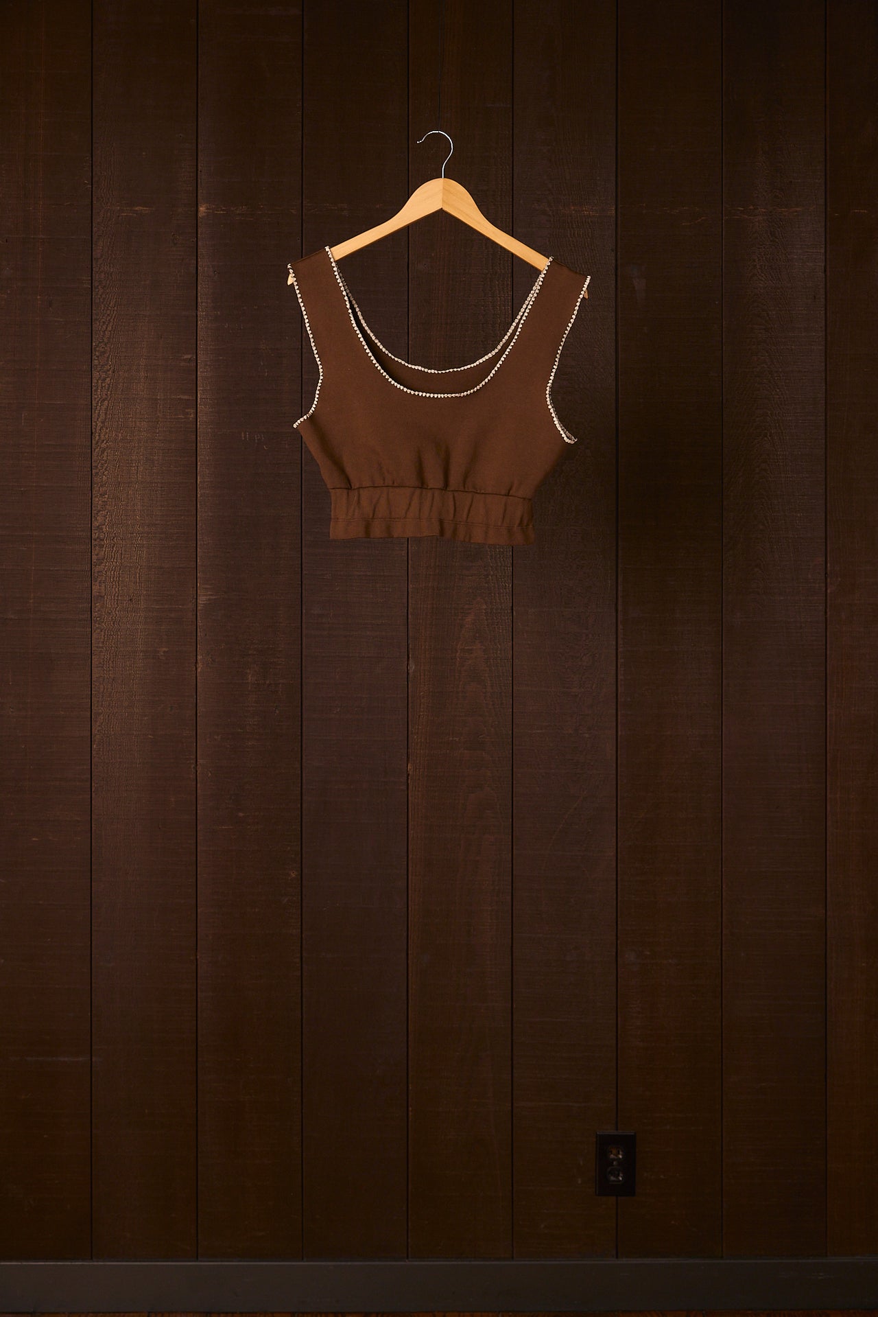 Brown crop top on a wooden hanger against a dark wooden wall.