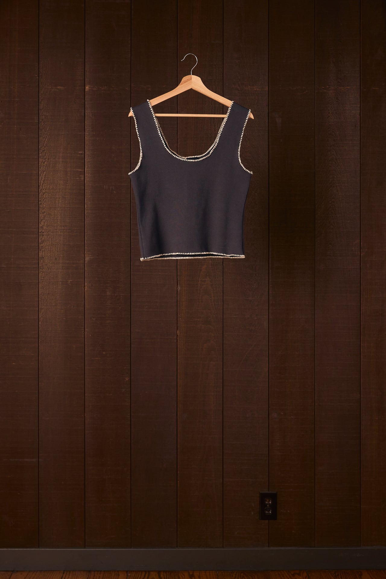 Black tank top on a wooden hanger against a wooden wall.