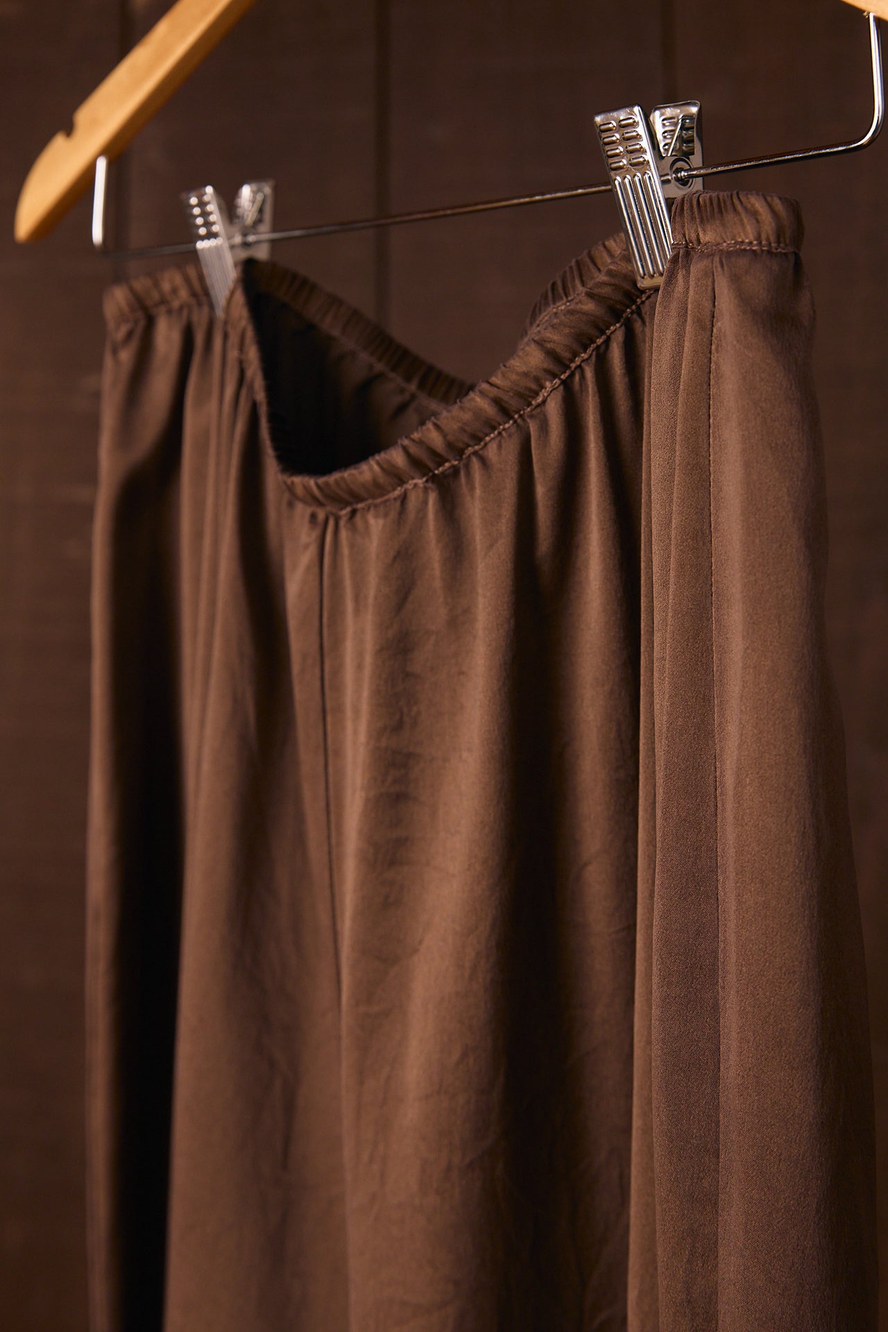 Brown pants hanging on a hanger against a brown tiled wall.