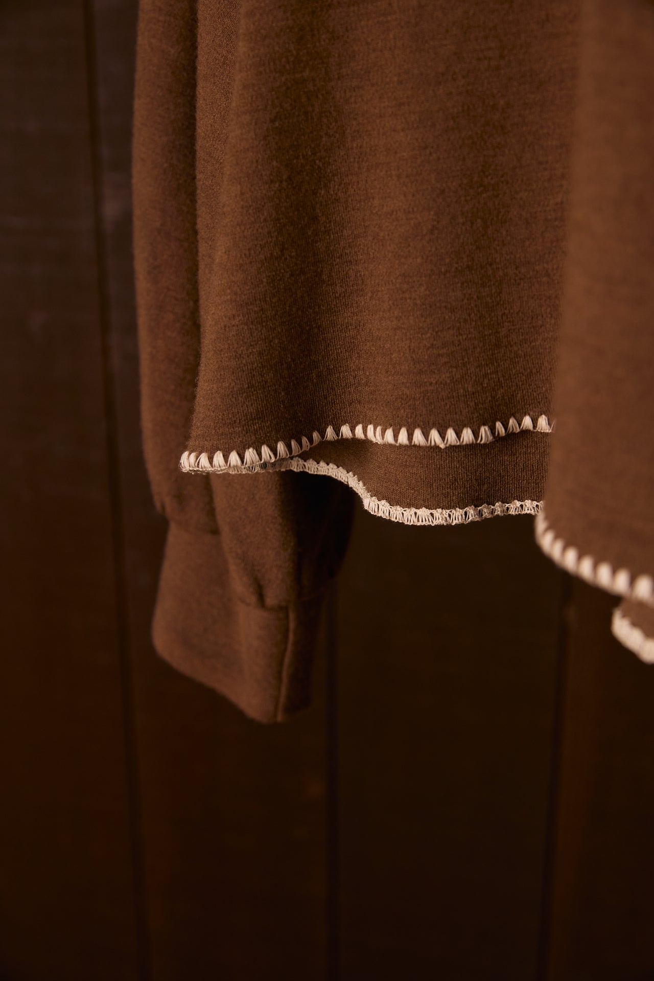 Brown wool garment with white Merrow Shell Stitch on a wooden surface