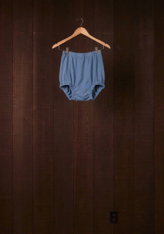 Indigo plant-dyed cotton Comfort Bloomer with scrunchie leg finish on a wooden hanger against a dark wood wall