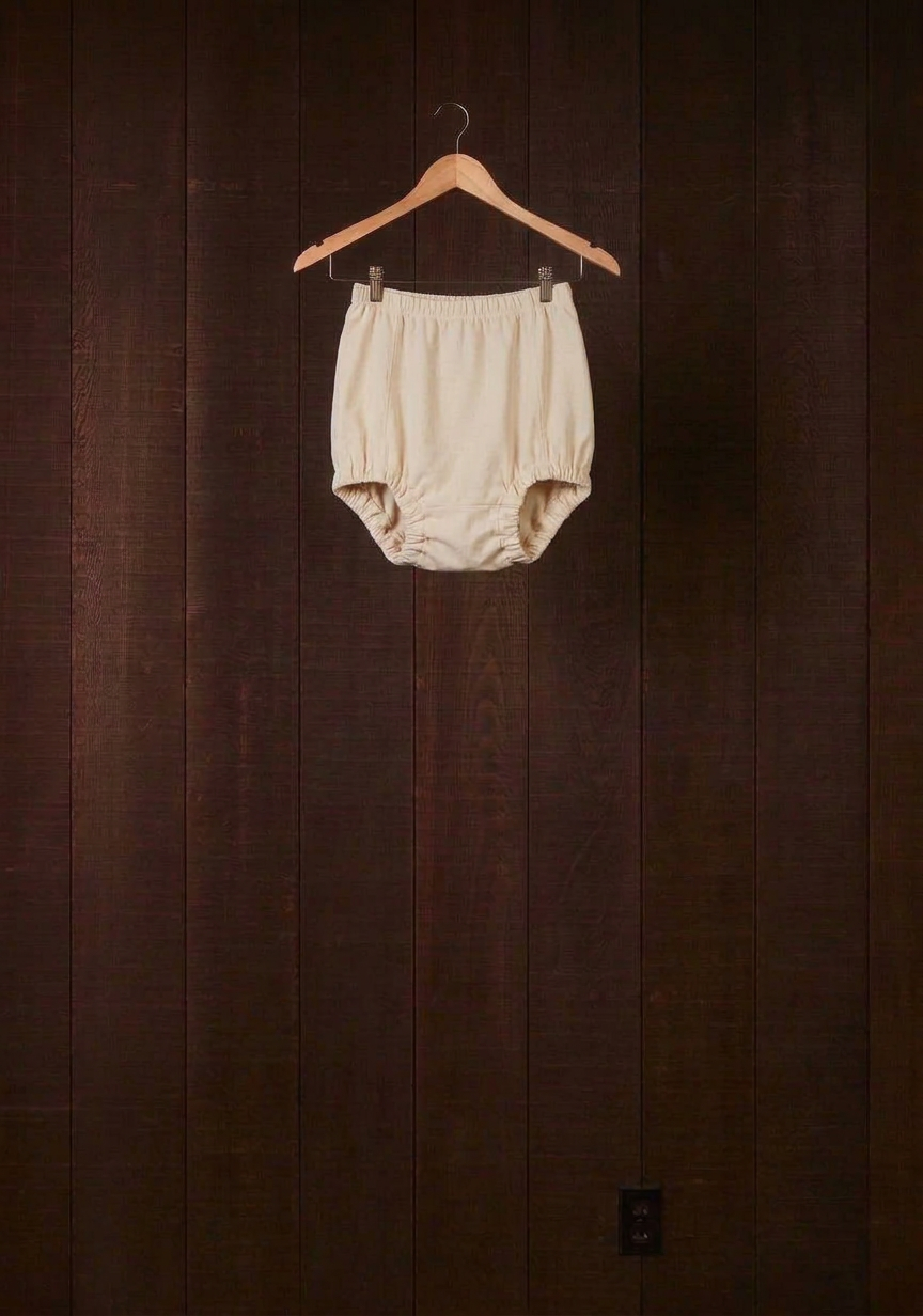 Undyed natural cotton Comfort Bloomer with scrunchie leg finish on a wooden hanger against a dark wood wall