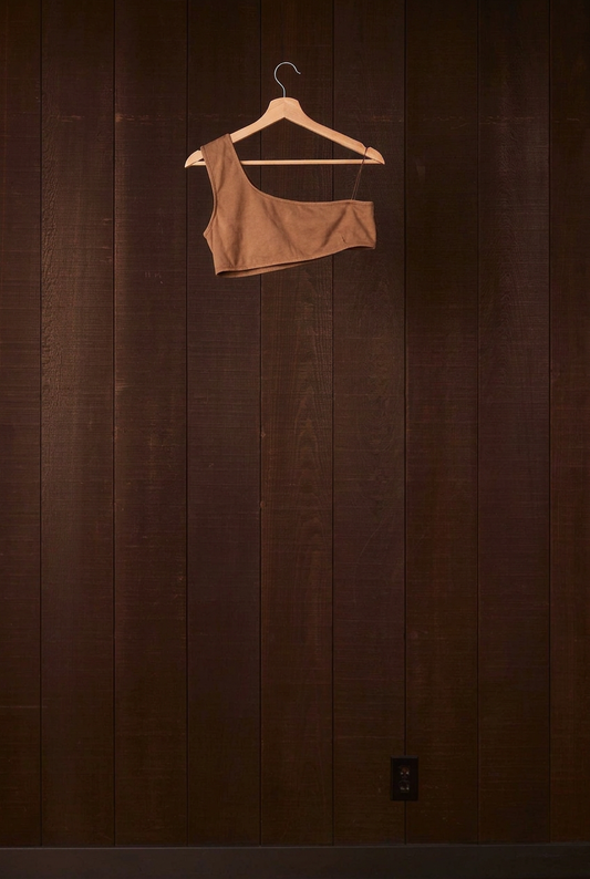 Cutch plant-dyed walnut cotton Una Bra on a wooden hanger against a dark wood wall