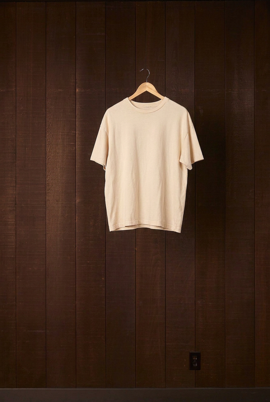 Undyed natural cotton jersey Den Shirt on a wooden hanger against a dark wood wall