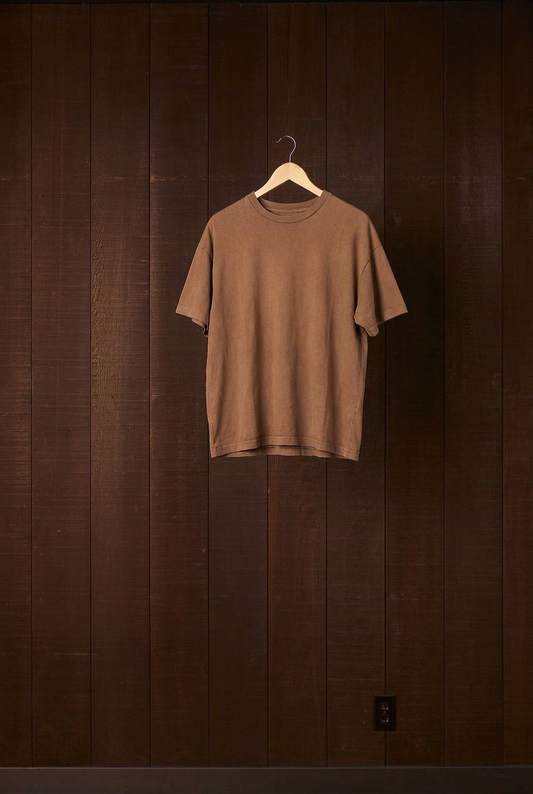 Cutch plant-dyed walnut cotton jersey Den Shirt on a wooden hanger against a dark wood wall