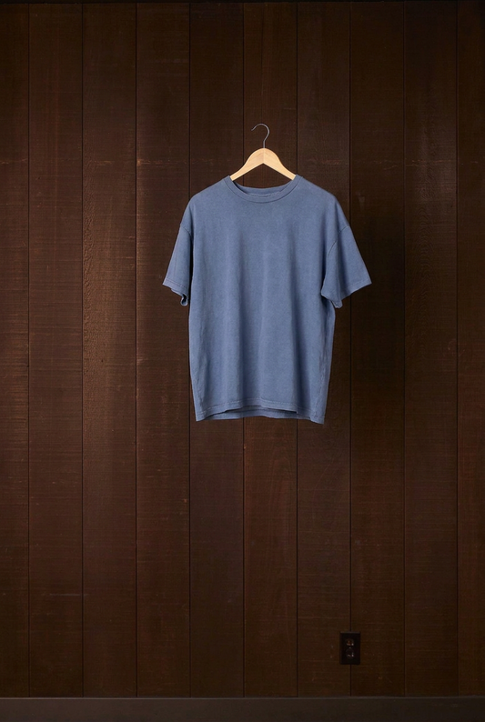 Indigo plant-dyed cotton jersey Den Shirt on a wooden hanger against a dark wood wall