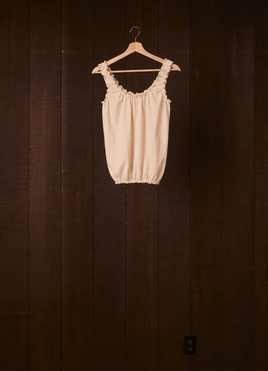 Undyed natural cotton jersey Cloud Camisoul on a wooden hanger against a dark wood wall